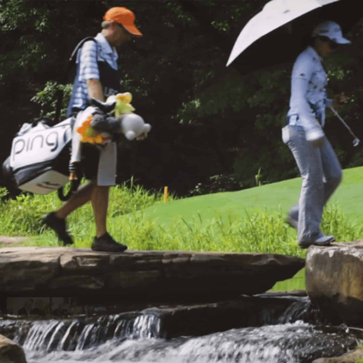 Player and caddie walking across rock waterfall