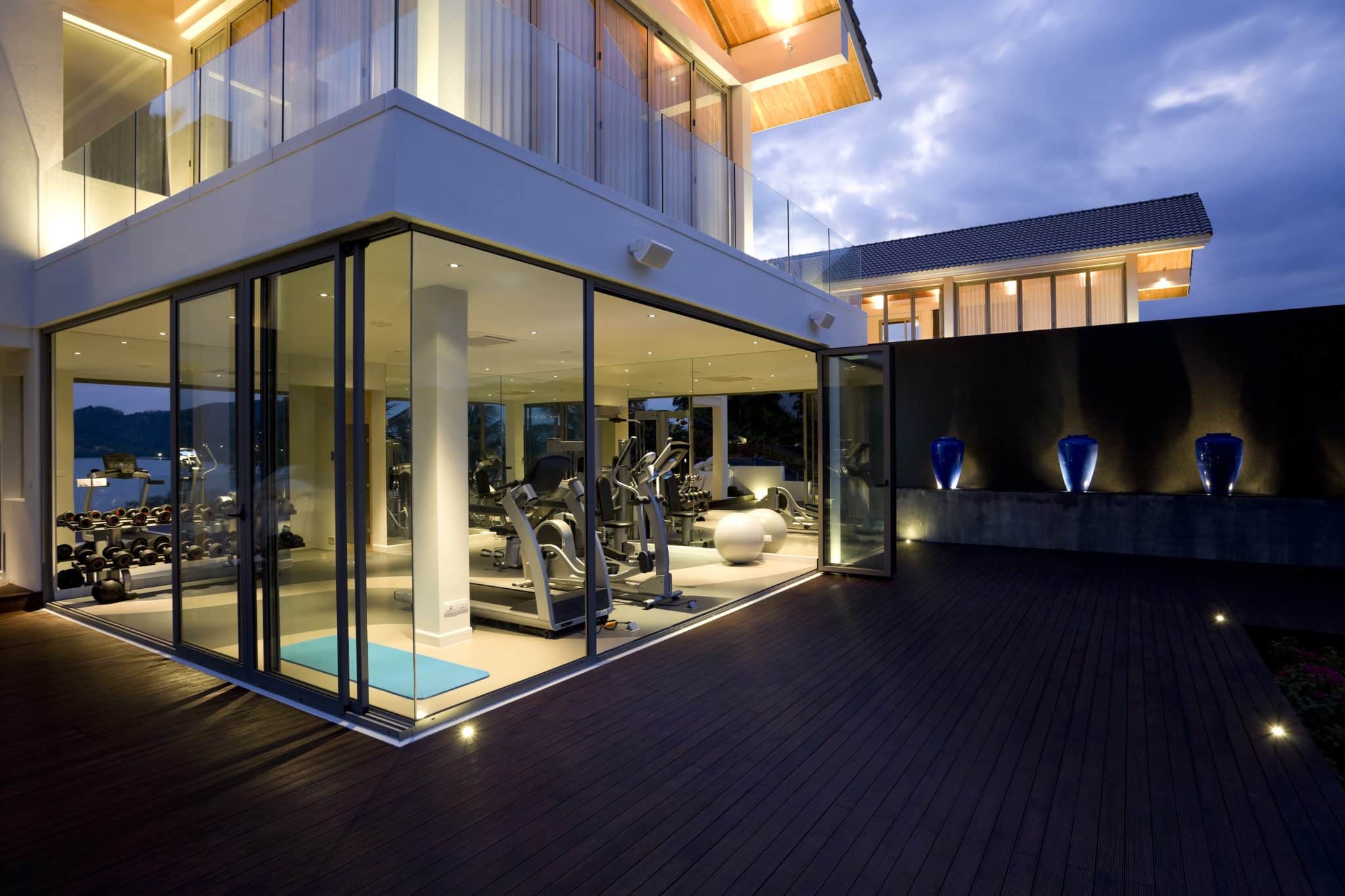 A luxury home gym design featuring outdoor views, access to a pool, high-end gym equipment, and other custom home elements.