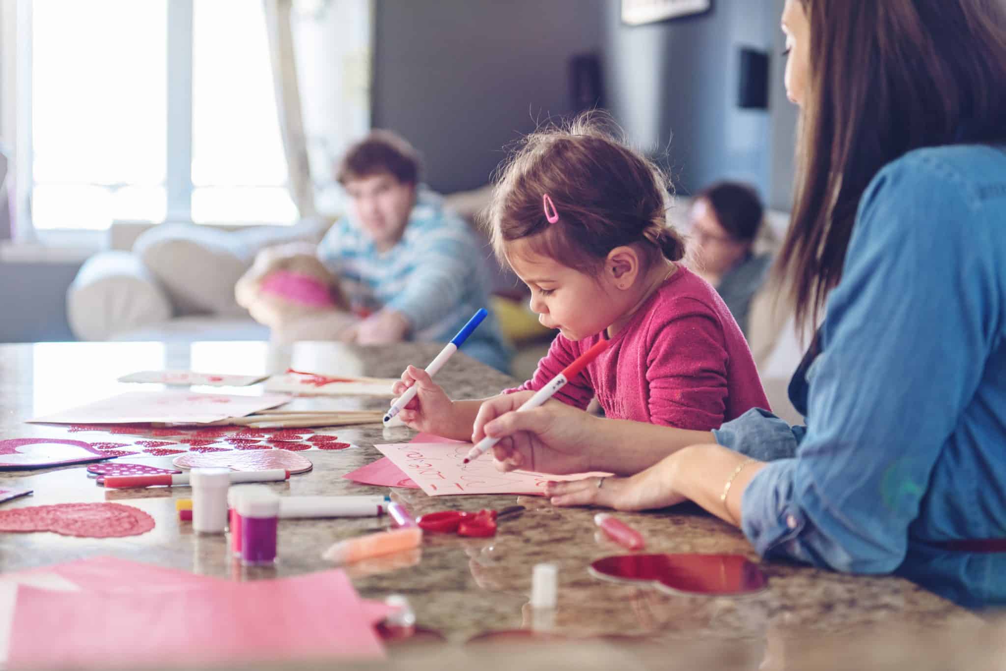 A young girl colors with her mom, who follows top home organization tips