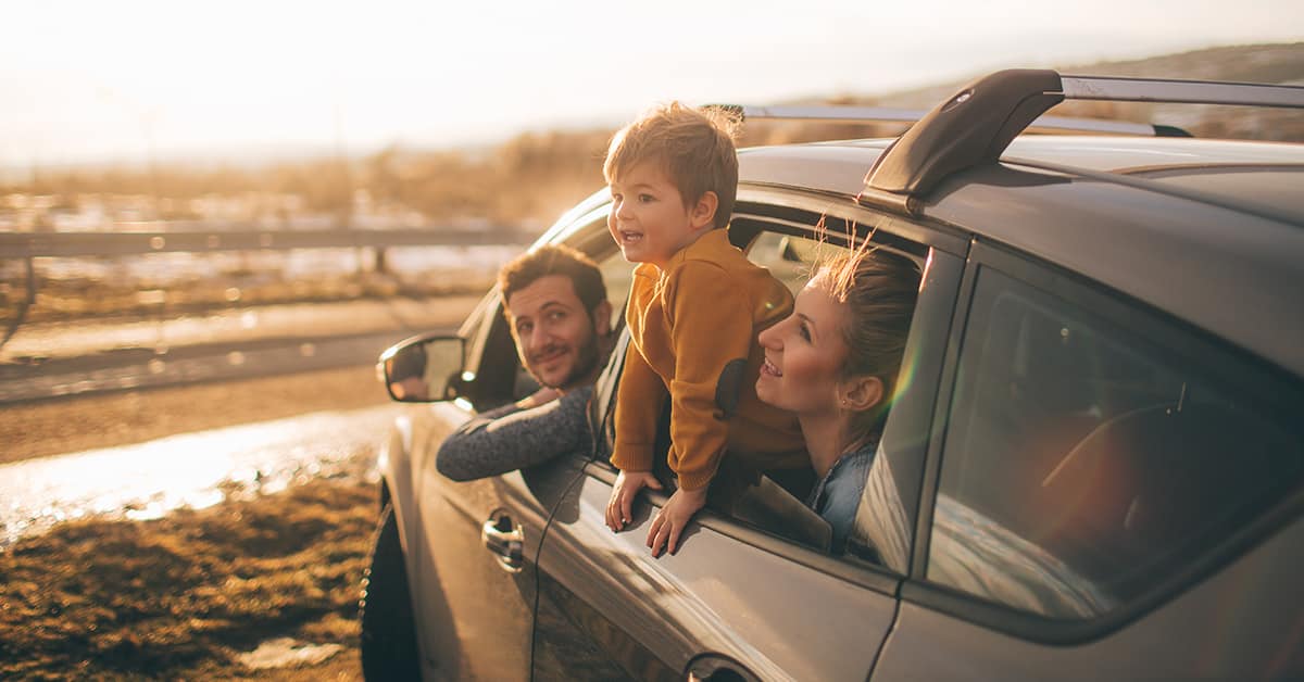 A dad, mom, and son lean out of the car window on a day trip