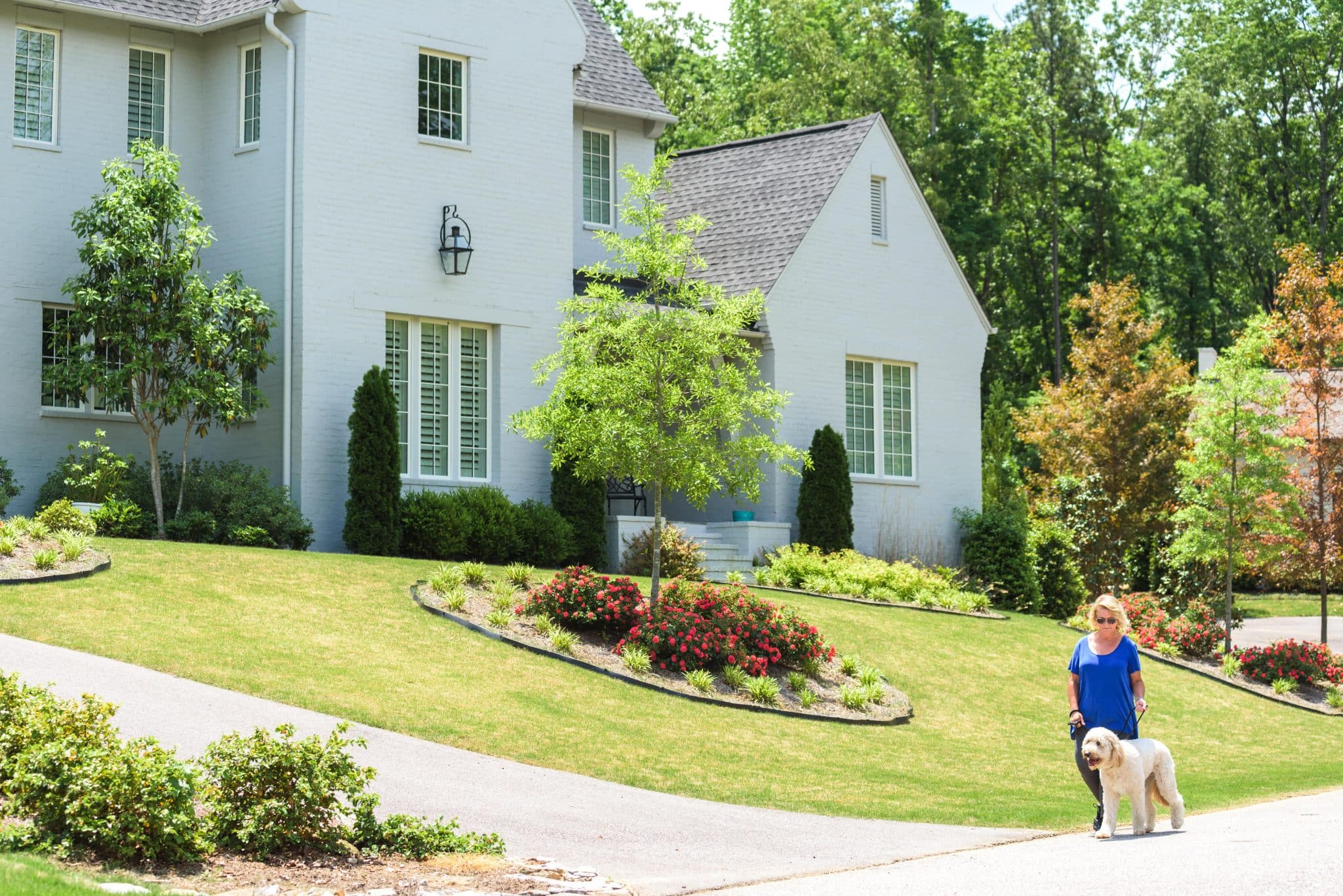 woman walking her dog down the sidewalk in front of a luxury home in Shoal Creek