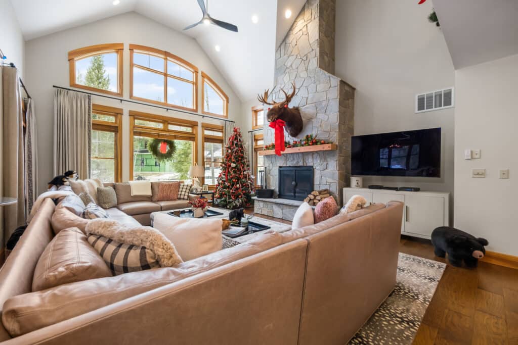 A beautiful living space home design idea with a vaulted ceiling, large TV, wraparound couch, and holiday decorations, perfect for hosting friends and family.