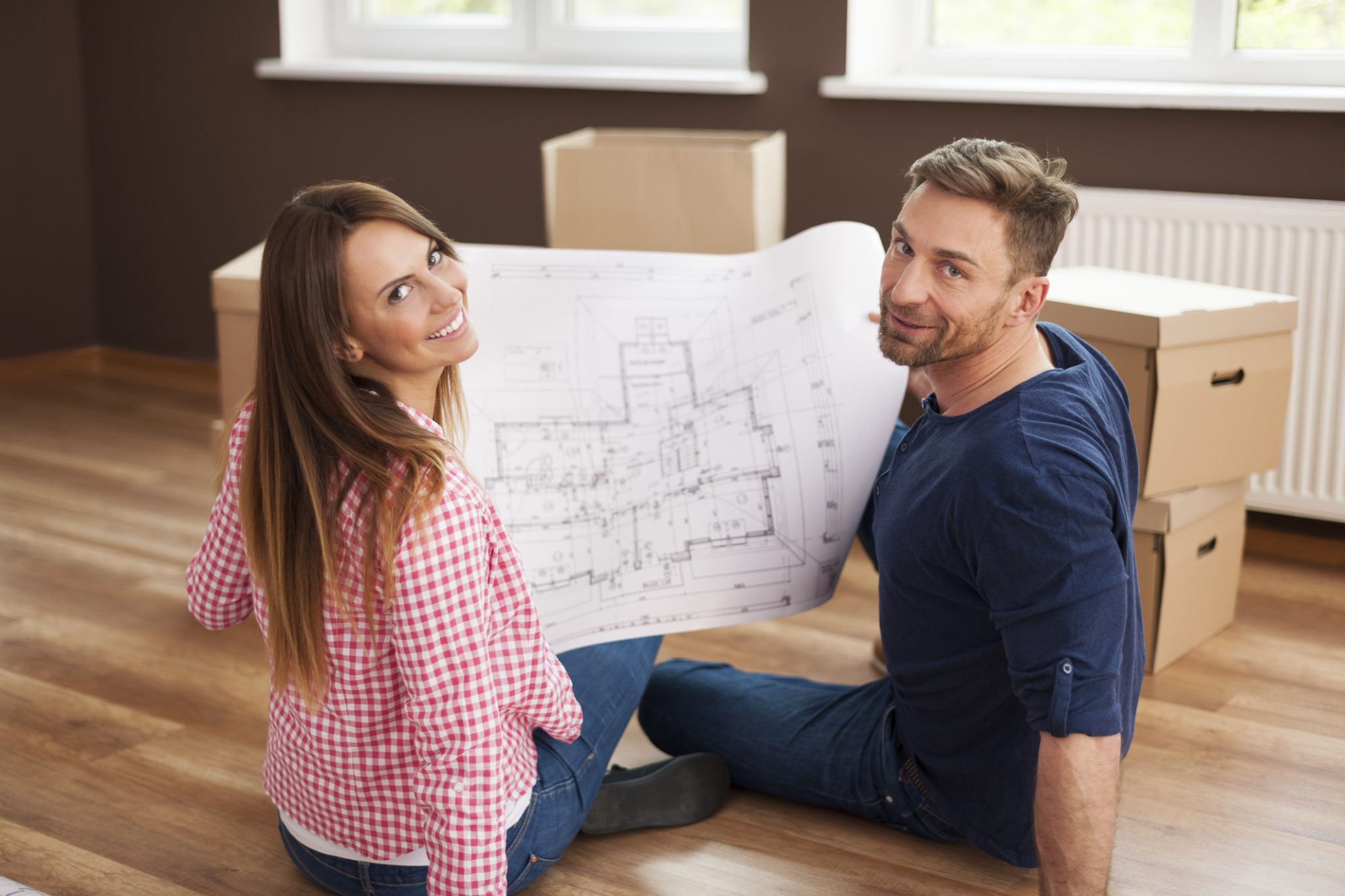 A couple sitting on the floor with blueprints that include all the most important luxury home design features.