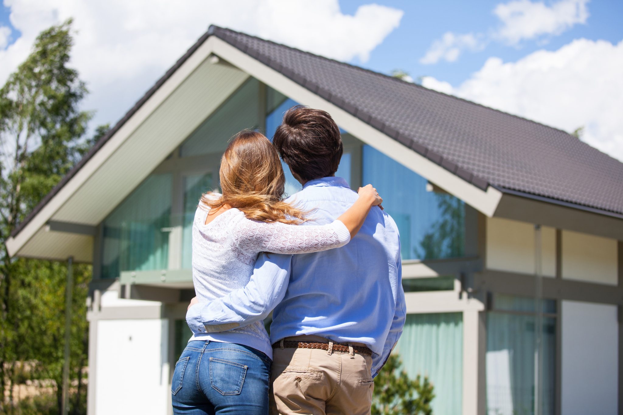 Photo of a couple facing away from the camera, admiring the exterior of their custom home.