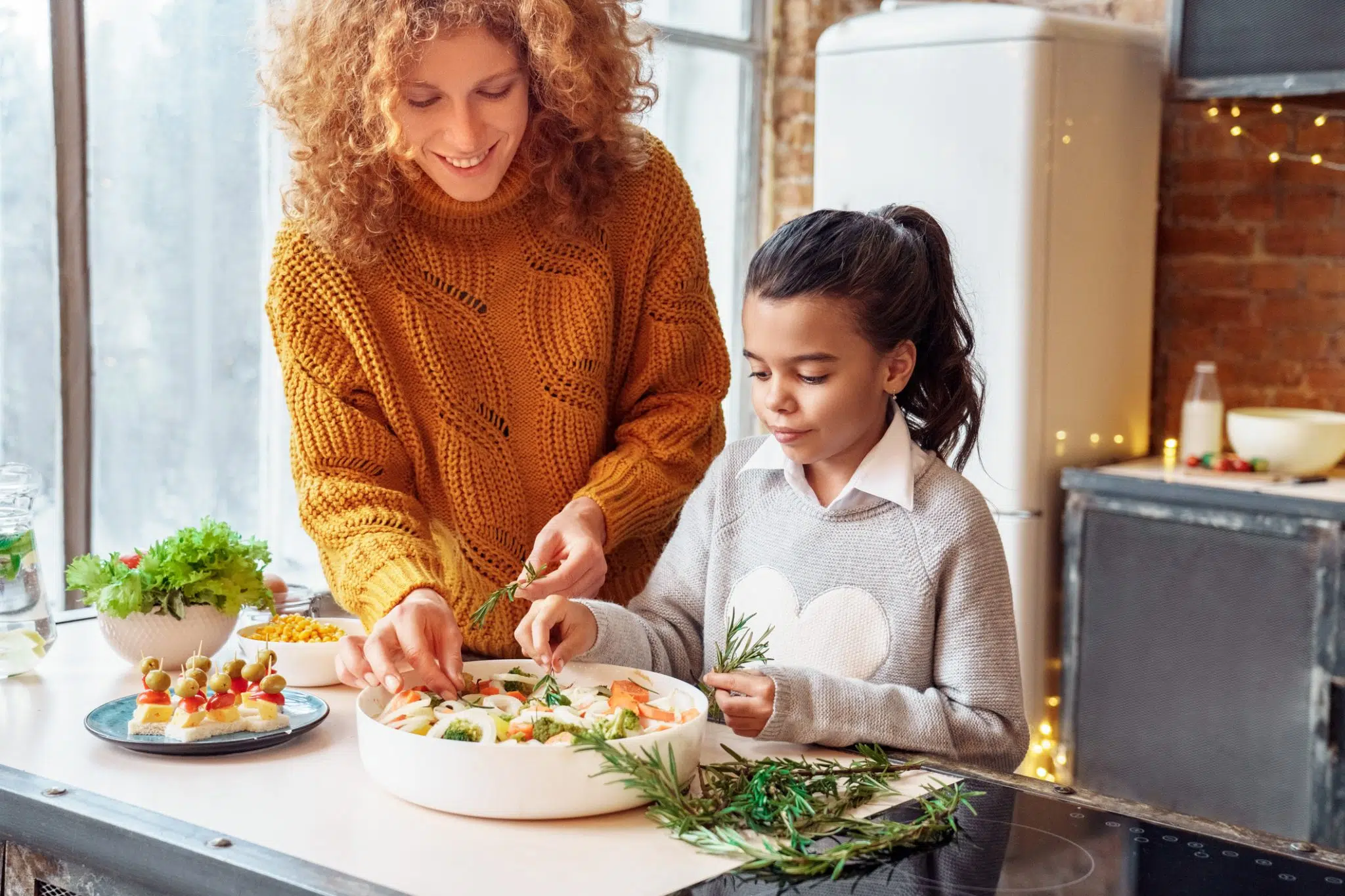 A woman and a young girl wearing cozy sweaters prepare food together as they get ready for the holidays.