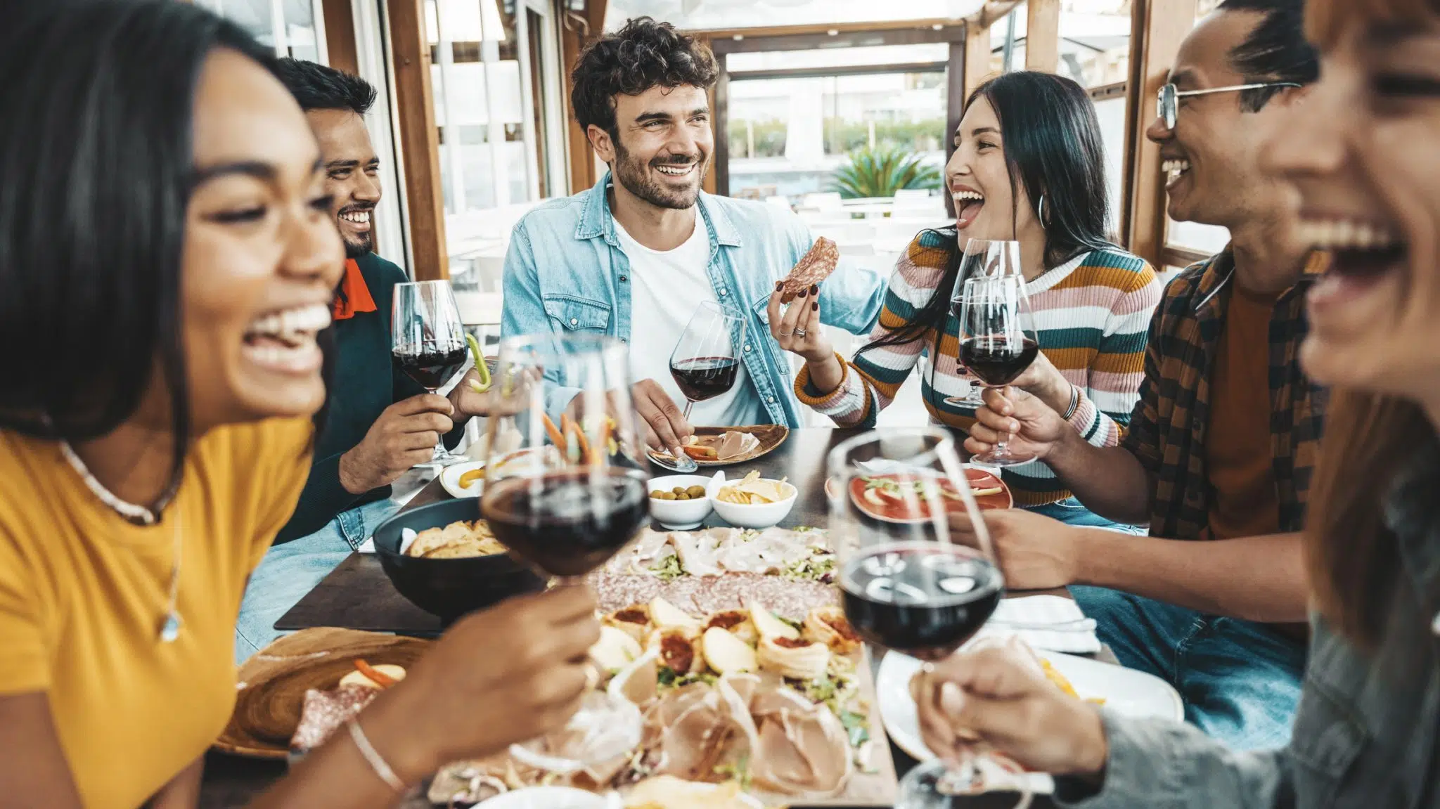 A vibrant group of young adults toasts glasses of wine and eats delicious food at a hot new restaurant, like the ones in Birmingham, AL.