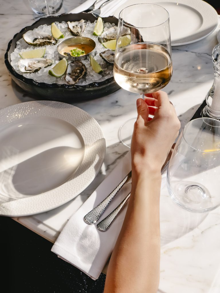 A person sitting at an empty place-setting with a glass of wine, waiting to be served oysters and other seafood.