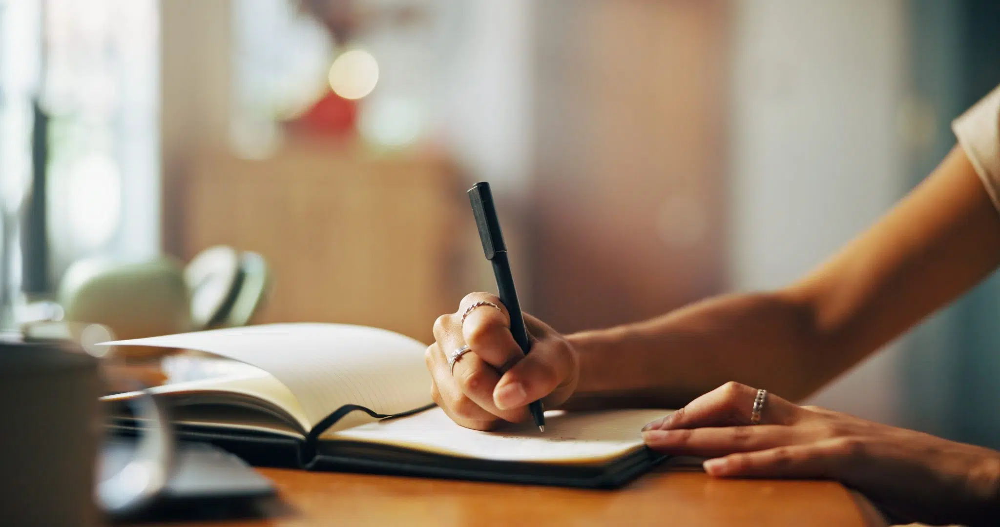A photo of a woman’s hand, holding a pen and writing in a notebook as she plans out new habits to put into action.