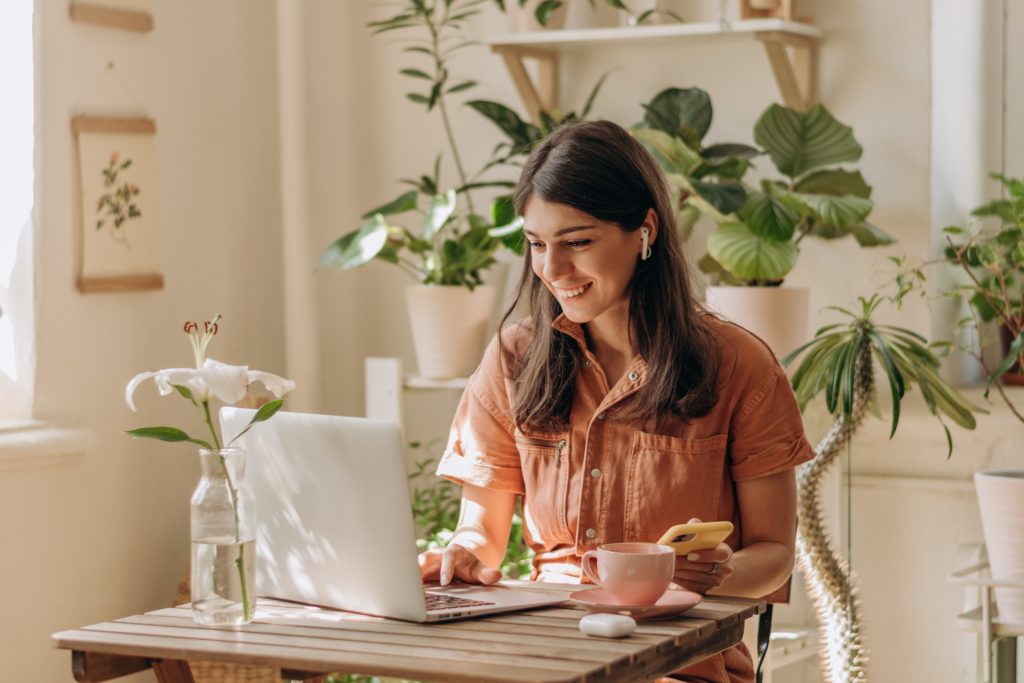 A young woman using a laptop a in her home office which she has decorated with plenty of green plants.