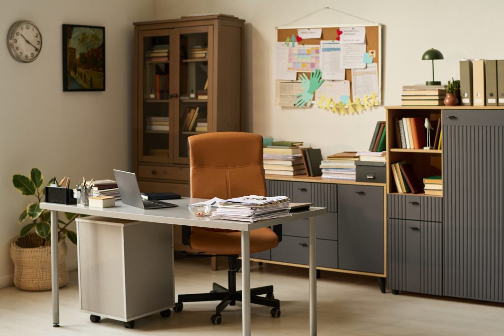 A modern home office with personalized decorations and plenty of storage behind the desk including glass-front and closed cabinets and drawers.