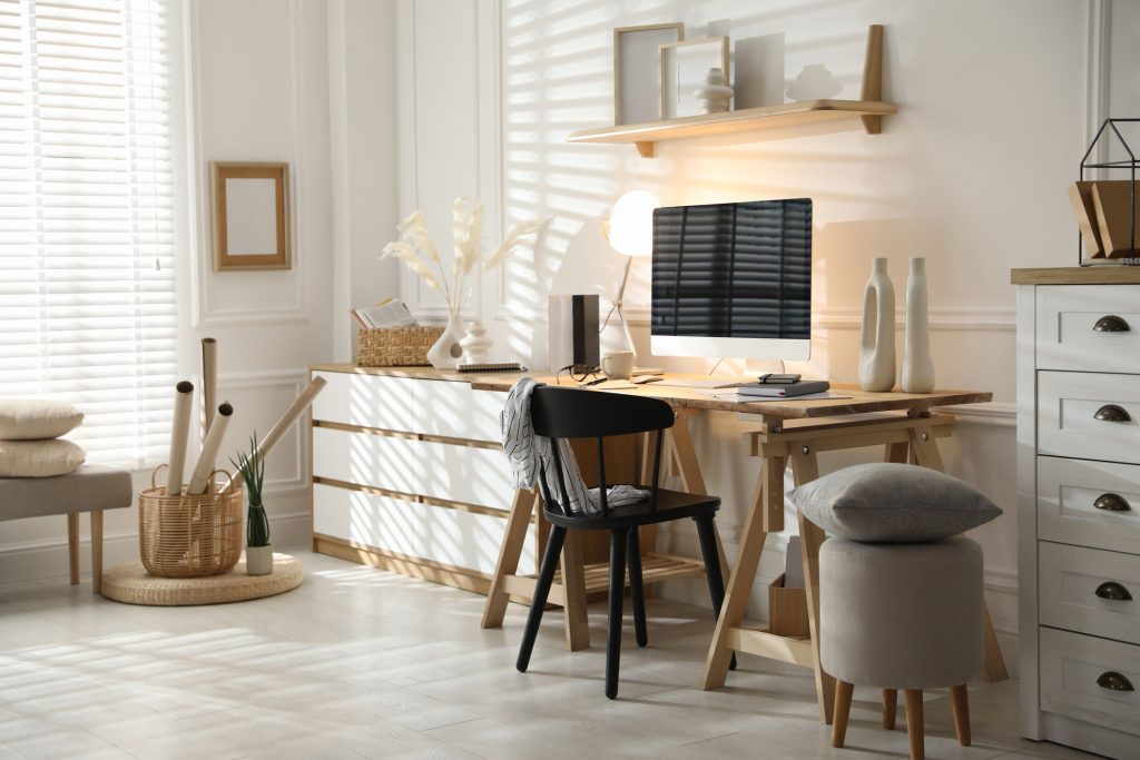 A bright, modern home office with natural and artificial lighting that creates a glare on the computer.