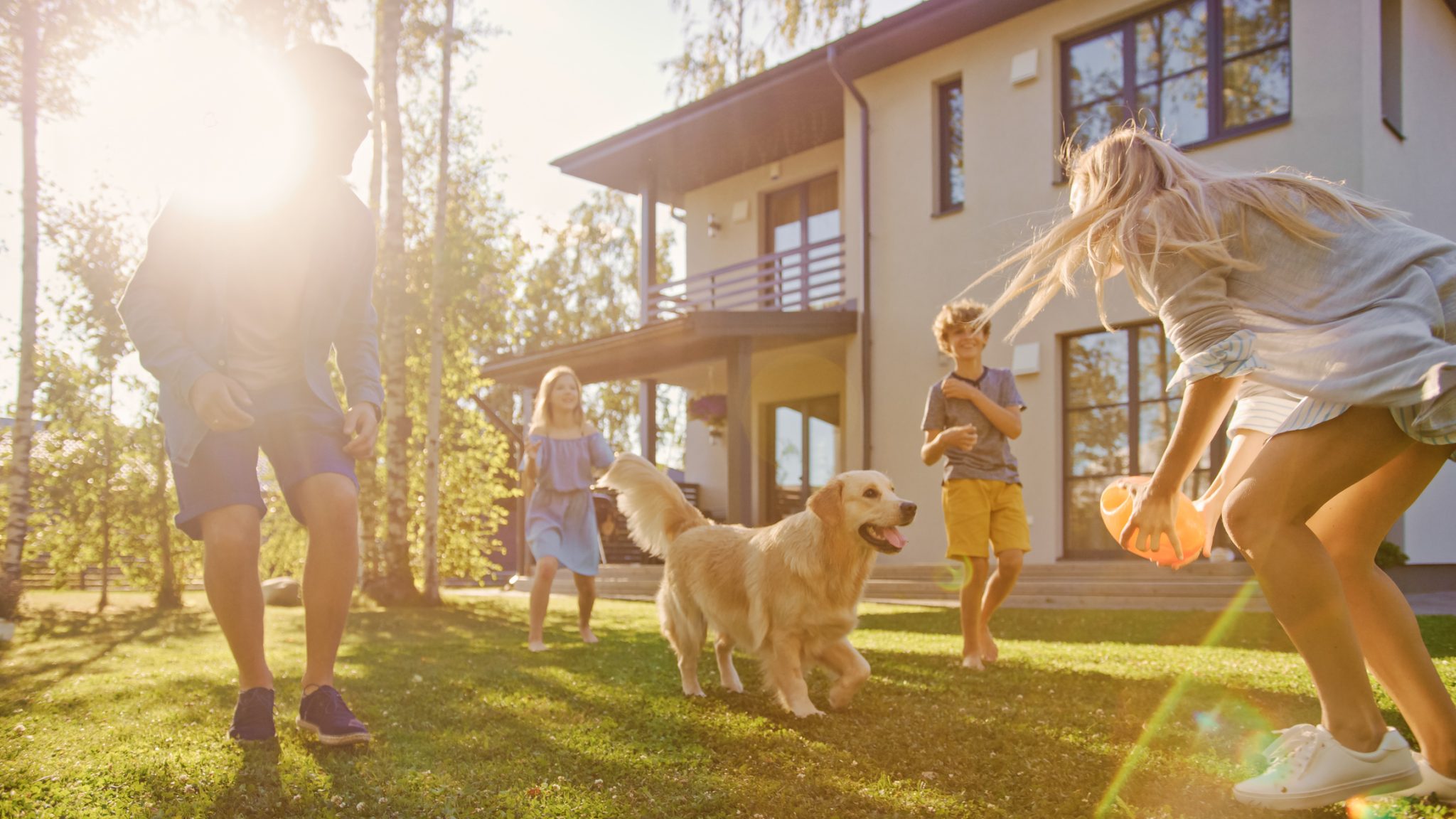 Family of four playing fetch with a golden retriever in a spacious backyard, enjoying outdoor living on a private home lot.