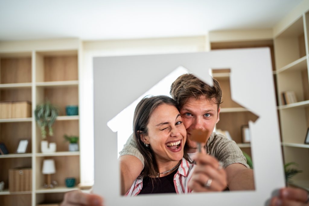 Happy couple holding house-shaped cutout and keys, having used a home tour checklist to find their new home.