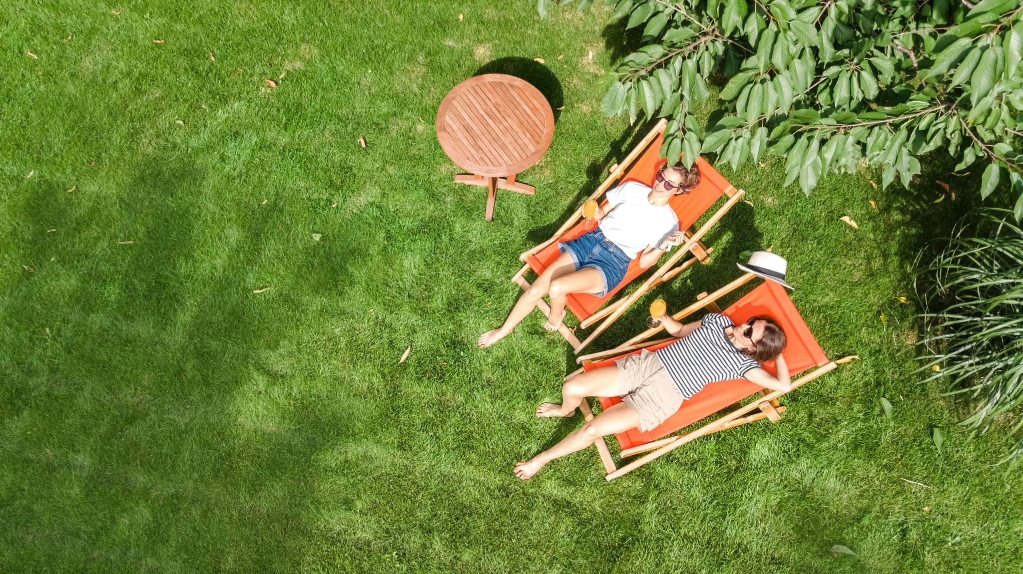 Aerial view of women relaxing on sunbed deckchairs in a wooded backyard, enjoying private outdoor space and secluded living.