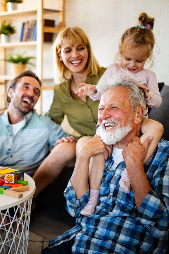 Smiling grandpa carrying granddaughter on his shoulders as adult children smile in a home built for aging in place
