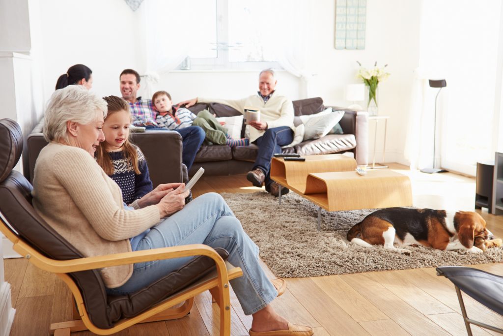 Grandparents, adult children, and grandchildren reading and talking together in a flexible family home living room