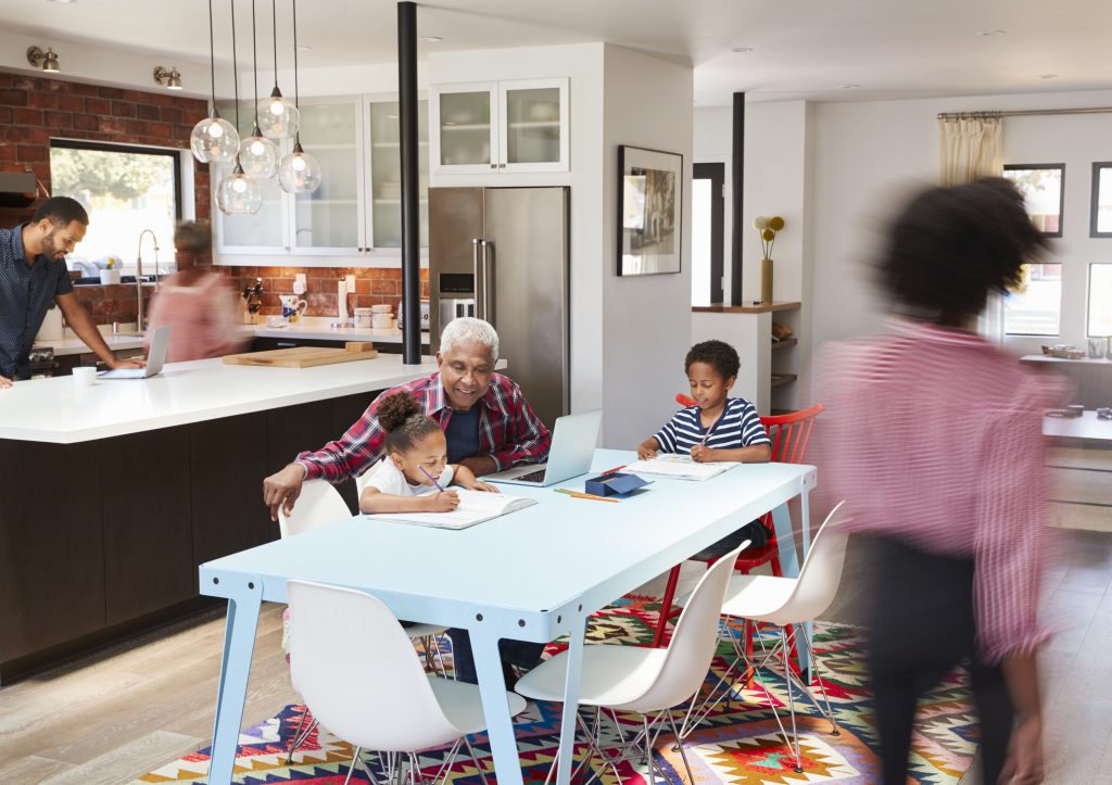 Dad and grandma cooking while grandpa helps kids with homework in an open kitchen of a multigenerational forever home